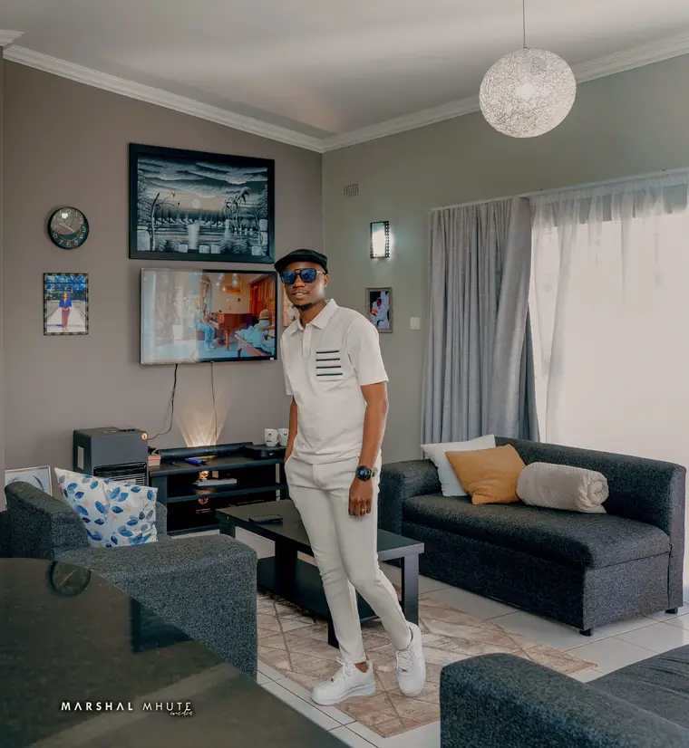 Wesley Mutsa Bangira, founder of Black Excellence, standing in a living room in white with a black cap and sunglasses